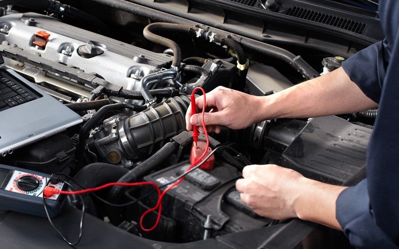 Mechanic using a multimeter to check a car battery in the engine bay